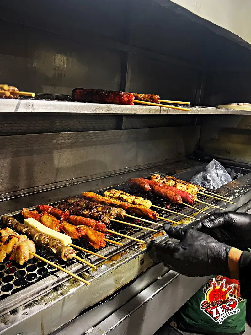 Churrasqueira cheia de espetinhos de frango, carne e linguiça
