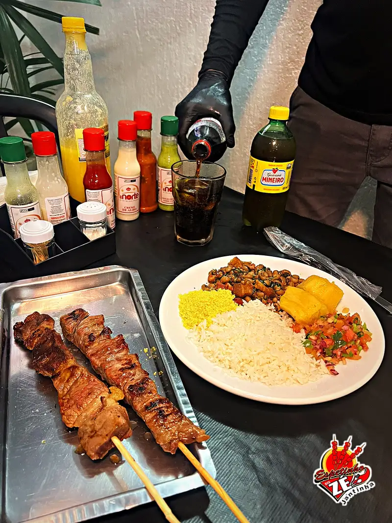 Jantinha completa com dois espetinhos de carne na bandeja e refrigerante sendo servido